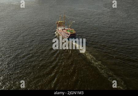 Piratenschiff im alten Stil, das ohne Segel im offenen Wasser in Richtung Sonne fährt Stockfoto