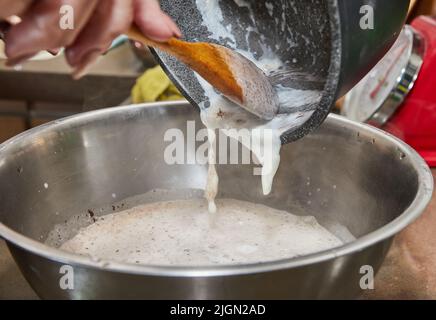 Der Koch gießt Schlagsahne in eine Schokoladenkuchenmischung mit Birnen und Nüssen. Schritt für Schritt Rezept Stockfoto