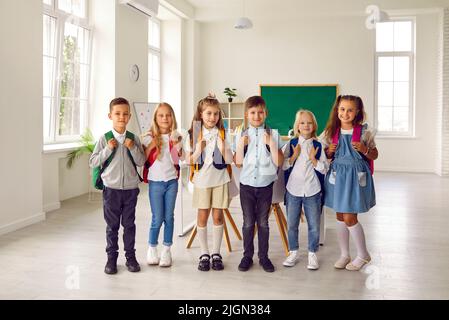 Porträt einer kleinen lächelnden Gruppe von Erstklässlern im modernen Klassenzimmer der Grundschule. Stockfoto