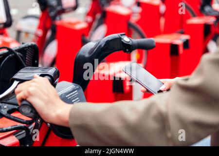 Hand mit Smartphone in einem Fahrradverleih Parkplatz Stockfoto