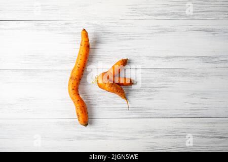 Zwei hässliche Karotten liegen auf einer hellen Holzoberfläche Stockfoto