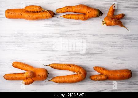 Hässliche Karotten liegen auf einer hellen Holzoberfläche Stockfoto