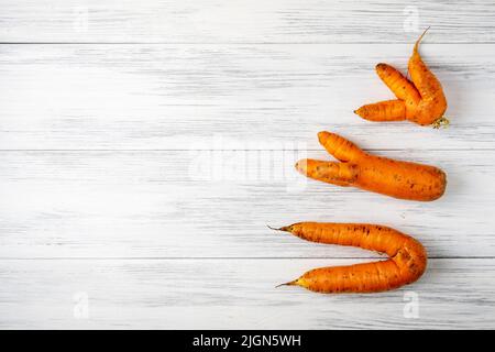 Hässliche Karotten liegen auf einer hellen Holzoberfläche Stockfoto