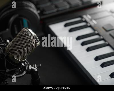 Auf dunkelgrauem Hintergrund ein professionelles Midi-Keyboard für Synthesizer, Studiokopfhörer und ein Studiomikrofon. Das Konzept ist ein Aufnahmestudio. Aufz Stockfoto