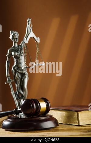 Auf einem dunkelbeigen Hintergrund eine bronzene Figur der Göttin der Gerechtigkeit Themis und ein hölzerner Richtergavel. Rechtsstaatlichkeit, Gericht, Justiz, Verfassung. Stockfoto