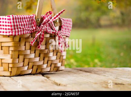 Auf einem Holztisch ein Strohpicknickkorb vor dem Hintergrund einer wunderschönen Herbstnatur. Picknick in der Natur, frische Luft, romantischer Spaziergang, Danksaggabe, h Stockfoto