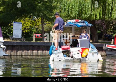 Rückansicht eines Motorbootes mit zwei Personen, die an einem Tag, an dem die Temperaturen auf 30 anstiegen, in Richtung Anlegestellen auf dem Fluss Ouse fahren. Ely, Cambridgeshire, Großbritannien Stockfoto