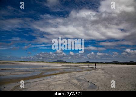 Eine Frau in einem roten Springer, die einen Hund am Gearraidh na Monadh Beach, South Uist (Uibhist a Deas) Stockfoto