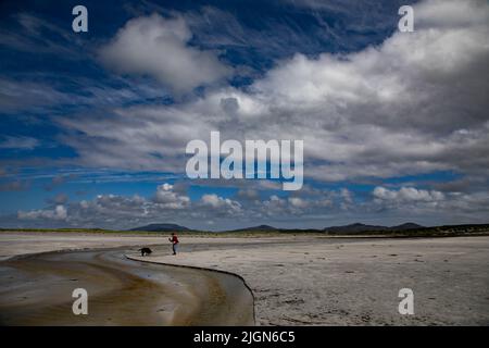 Eine Frau in einem roten Springer, die einen Hund am Gearraidh na Monadh Beach, South Uist (Uibhist a Deas) Stockfoto