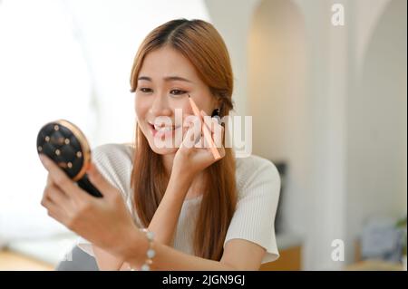 Schöne elegante tausendjährige asiatische Frau oder weibliche Beauty-Bloggerin, die ihr Make-up macht, mit Augenlinse. Stockfoto