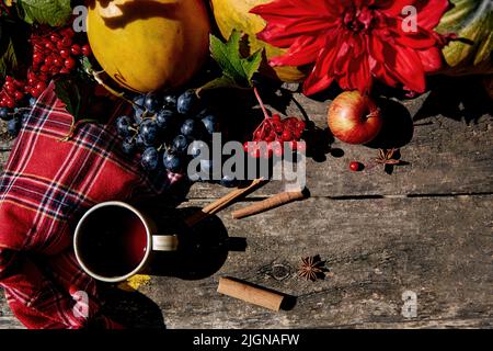 Rustikales gemütliches Stillleben mit Trauben, Viburnum, Mais, Kürbismelone, Äpfeln und roten Dahlien. Gemütliches Zuhause mit einer warmen Tasse Tee. Thanksgiving Day Konzept. Herbstliches ästhetisches Konzept. Hochwertige Fotos Stockfoto