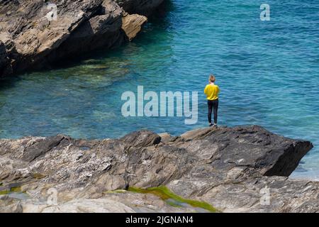 Eine Frau, die allein auf Felsen steht, die von einer Ebbe an der Küste bei Fistral in Newquay in Cornwall in Großbritannien freigelegt wurden. Stockfoto