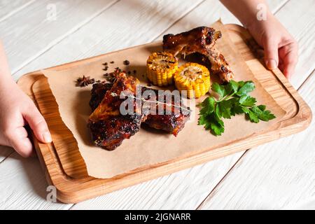 Hände nehmen Holztablett mit Grill vom Tisch Stockfoto