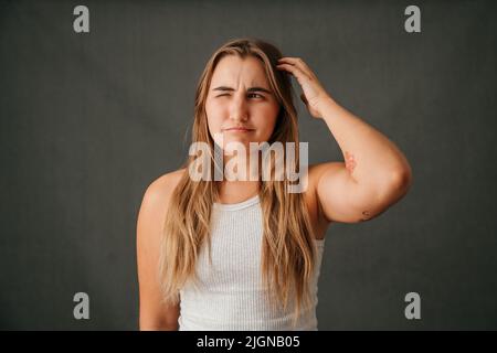 Junge blonde Frau kratzt sich am Kopf und denkt nach Stockfoto