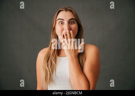 Junge blonde Frau, die ihre Hand über den Mund legt, überrascht Stockfoto