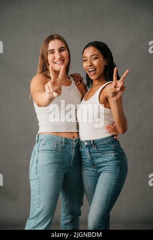 Zwei Freundinnen lächelten und zeigten das Friedensschild in Jeans und Tank Tops Stockfoto