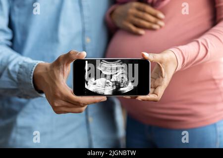 Schwarzes trächtiges Paar hält Smartphone mit Baby-Ultraschallbild, Nahaufnahme Stockfoto