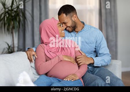 Portrait eines liebevollen, schwanger schwarzen muslimischen Paares, das sich auf der Couch entspannt Stockfoto