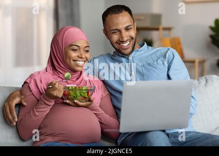 Glücklich Schwanger Muslim Paar Entspannen Mit Laptop Im Wohnzimmer Stockfoto