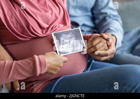 Unkenntlich Schwanger Muslim Paar Hält Baby Sonographie Bild Beim Entspannen Auf Der Couch Stockfoto