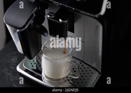 Frisch gebrühter Cappuccino wird aus der Kaffeemaschine in Glasküken gegossen. Professionelle Cappuccino-Zubereitung zu Hause. Stockfoto