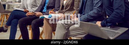 Beine Menschen in Bürokleidung sitzen drinnen und Notizen in Papieren und Laptop während der Sitzung Stockfoto