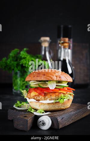 Hamburger mit Hähnchenburger Fleisch, Käse, Tomaten, Gurken und Salat auf Holzboden. Leckerer Burger. Nahaufnahme Stockfoto