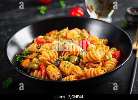 Klassische italienische Pasta fusilli marinara mit Muscheln, grünen Oliven und Kapern auf dunklem Tisch. Fusilli Pasta mit Sauce Marinara Stockfoto