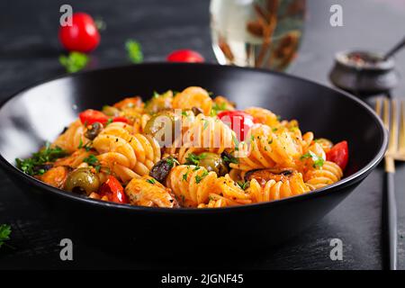 Klassische italienische Pasta fusilli marinara mit Muscheln, grünen Oliven und Kapern auf dunklem Tisch. Fusilli Pasta mit Sauce Marinara Stockfoto