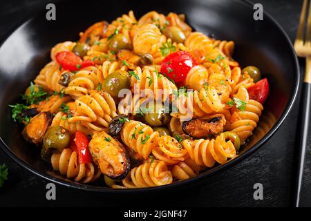 Klassische italienische Pasta fusilli marinara mit Muscheln, grünen Oliven und Kapern auf dunklem Tisch. Fusilli Pasta mit Sauce Marinara Stockfoto