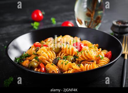 Klassische italienische Pasta fusilli marinara mit Muscheln, grünen Oliven und Kapern auf dunklem Tisch. Fusilli Pasta mit Sauce Marinara Stockfoto