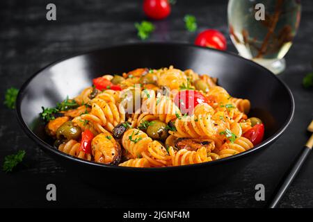 Klassische italienische Pasta fusilli marinara mit Muscheln, grünen Oliven und Kapern auf dunklem Tisch. Fusilli Pasta mit Sauce Marinara Stockfoto