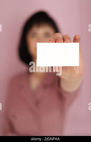 Geschäftsfrau, die eine leere Visitenkarte vorführt und überreicht. Hände mit einer weißen Visitenkarte, einem Geschenk, einem Ticket, einem Pass, einer Nahaufnahme auf verschwommenem BL Stockfoto
