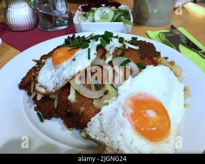 Schnitzel, deutsch oder wiener, top mit sonnigen Seiteneiern und gebackenen Kartoffeln, garniert mit Zwiebel und grünen frischen Frühlingszwiebeln, da kann man nie falsch machen. Stockfoto