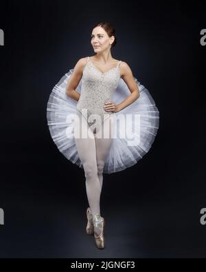 Attraktive Ballerina posiert anmutig im Studio auf schwarzem Hintergrund Stockfoto