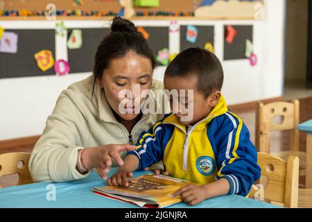 (220712) -- LHASA, 12. Juli 2022 (Xinhua) -- Eine Lehrerin lehrt Huo Dangsheng (R), am 22. März 2022 in einem Kindergarten im Kreis Gonggar, Stadt Shannan, südwestlich der Autonomen Region Tibet, ein Buch zu lesen. (Xinhua/Zhou Dixiao) Stockfoto