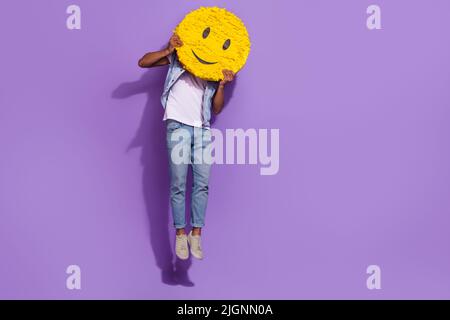 In voller Länge Foto von positiven fröhlichen Mann tragen Jeans springen leeren Raum halten Lächeln Pinata isoliert violette Farbe Hintergrund Stockfoto