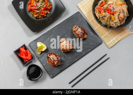 Teriyaki Huhn mit Sesam auf einem Serverboard. Asiatische Küche. Reisnudeln und Gemüse auf grauem Hintergrund Stockfoto