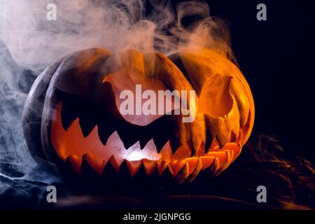 Komposition aus halloween geschnitztem Kürbis mit Rauch und orangefarbenem Licht auf schwarzem Hintergrund Stockfoto