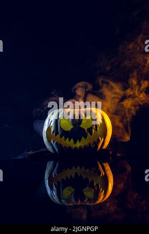 Komposition aus halloween geschnitztem Kürbis mit Rauch und orangefarbenem Licht auf schwarzem Hintergrund Stockfoto