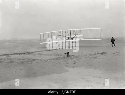 Vintage-Foto vom 17. 1903. Dezember des Wright Flyer auf seinem ersten motorisierten und kontrollierten Flug von Orville Wright mit seinem Bruder Wilbur Wright an der Seite der Maschine. Der erste Flug fand in Kitty Hawk, North Carolina, USA, statt Stockfoto