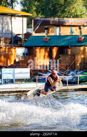 Ein Athlet-Wakeboarder wirft viele Spritzer auf das Wasser, indem er Tricks ausführt und mit den Händen am Seil hält. 06.19.1922. Kiew. Ukraine. Stockfoto