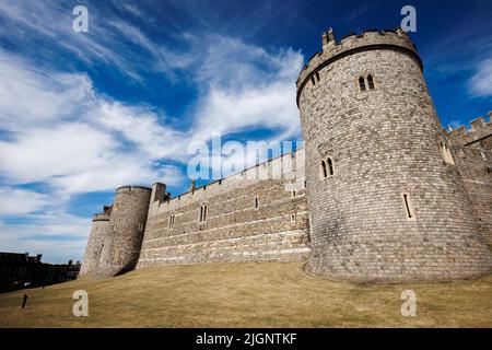 Eine dramatische Blickwinkelaufnahme von der Steinmauer und dem Rundturm von Windsor Castle vor einem blauen Himmel mit fahnenförmigen Wolken, Berkshire, England. Stockfoto