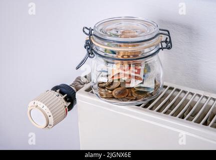 Sparen beim Heizen: Heizkörper und Thermostat mit Sparschwein und Geld Stockfoto