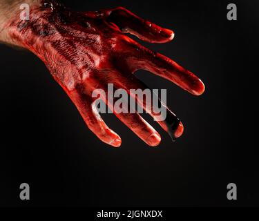 Nahaufnahme einer mit Blut befleckten männlichen Hand auf schwarzem Hintergrund. Stockfoto