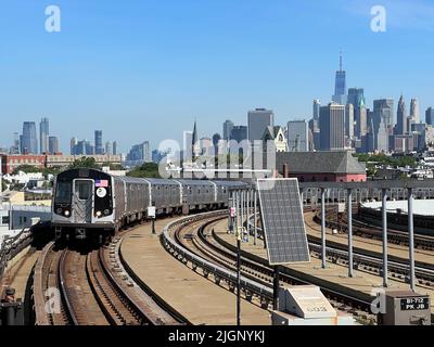 F-Zug-Linie, die in die Smith Ninth Street erhöhte U-Bahn-Station in Brooklyn mit einem klaren Blick auf die Skyline von Lower Manhattan kommt. Stockfoto