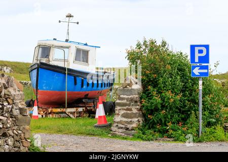 Parkschild und Pfeil auf einem Metallabzug mit einem alten Fischerboot auf einem Anhänger im Hintergrund Stockfoto