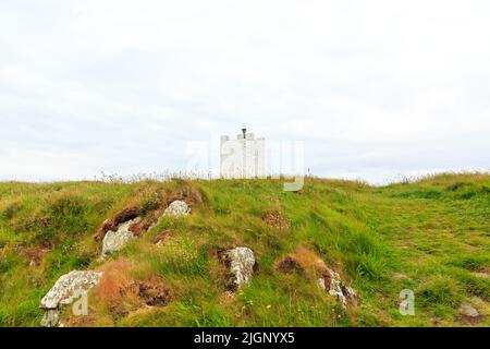 The , Isle of Whithorn, Schottland - 13. Juni 2022: Isle Head Lighthouse aus einem niedrigen Winkel mit Felsen und Gras im Vordergrund Stockfoto