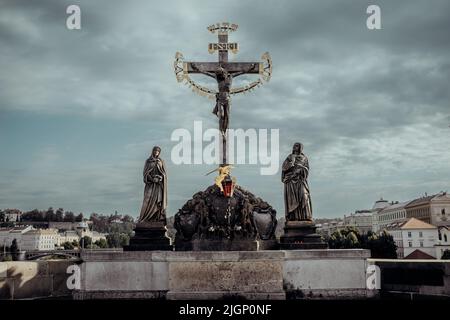 Bedeutendes Denkmal - Statue des gekreuzigten Christus auf der Karlsbrücke in Prag. Kreuzigungsstatue aus dem 17.. Jahrhundert mit hebräischem Schriftzug. Altstadt. Stockfoto