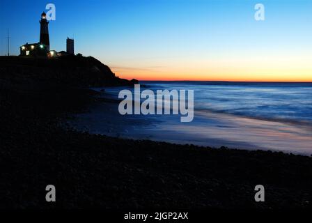 Der Sonnenaufgangshimmel macht den Montauk Point Lighthouse, an der östlichen Spitze von Long Island, New York, in Silhouette, während er sich im Meerwasser spiegelt Stockfoto